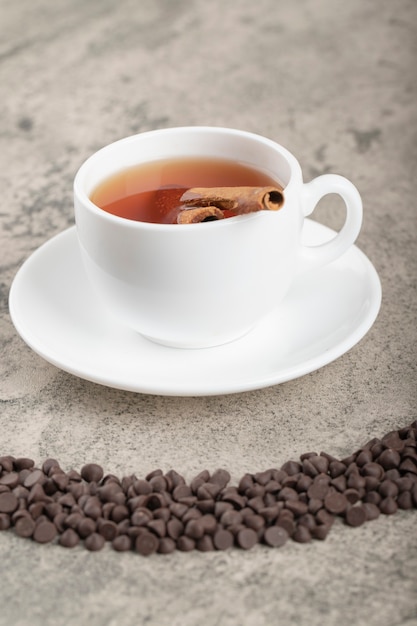Stapel van donkere chocoladeschilferdruppels en kopje zwarte thee op tafel.