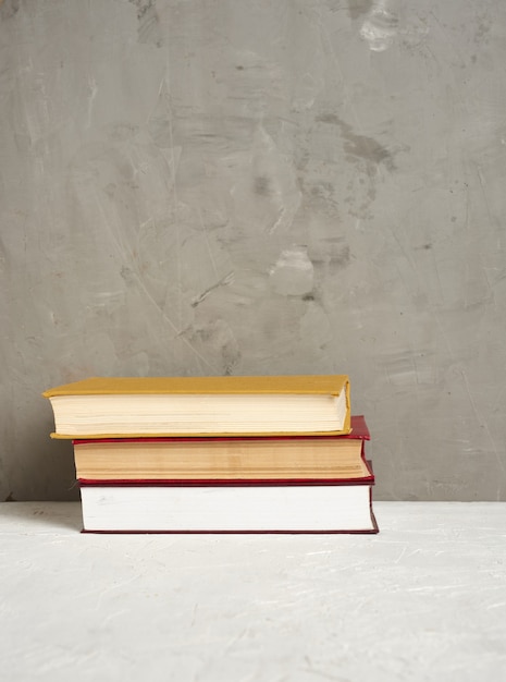 Stapel verschillende hardcover boeken tegen betonnen muur