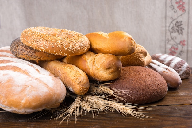 Stapel verschillende soorten gebakken broodbroden, baguettes, bagels en broodjes bovenop volkoren stengels boven houten tafel