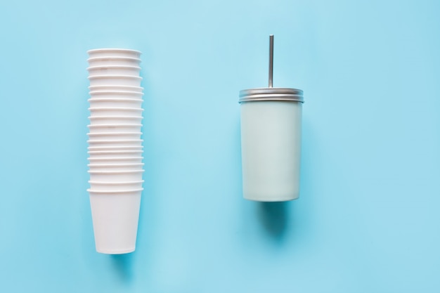 Stapel wegwerp witte kopjes wekelijks gebruik en tegengewicht herbruikbare mok voor drankjes dagelijks gebruik op blauw