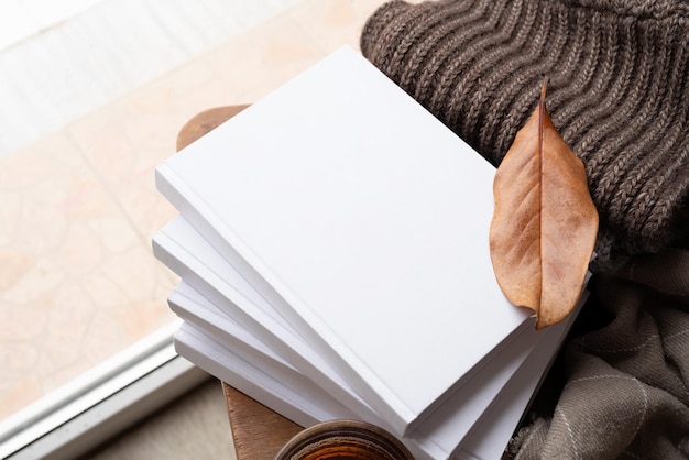 Stapel witte blanco boeken met herfstbladeren en een kop hete thee op een oud houten stoelmodel