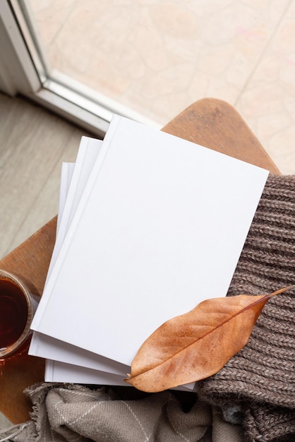 Stapel witte blanco boeken met herfstbladeren en een kop hete thee op een oud houten stoelmodel