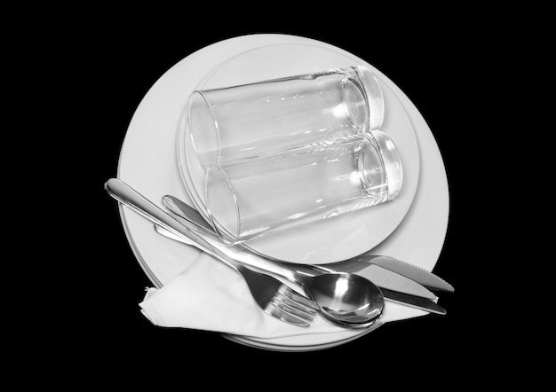 Stapel witte borden, glazen met vorken en lepels op zijden servet. Zwarte achtergrond