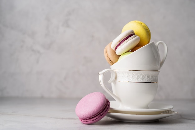 Stapel witte koffiekopjes gevuld met bitterkoekjes op de rand van de tafel, witte bakstenen muur achtergrond