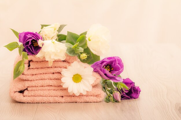 Stapel zachte badstof handdoeken met witte en violette bloemen op roze achtergrond.