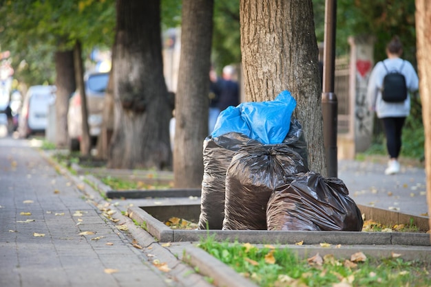 Stapel zwarte vuilniszakken vol afval achtergelaten voor ophalen aan straatkant. prullenbak verwijdering concept.