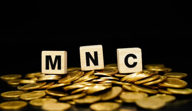 Stapels gouden munten met de letters MNC (Multi National Corporation) op een houten kubus.