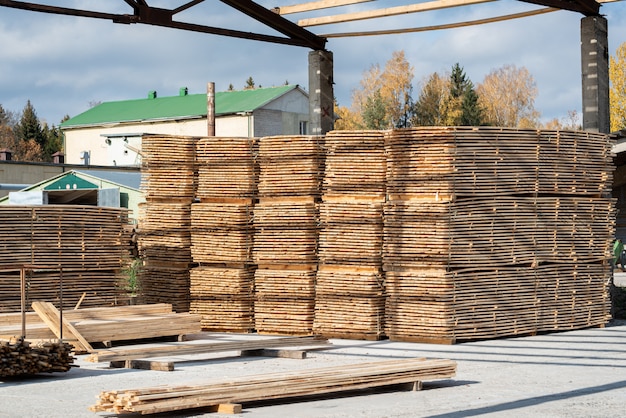 Stapels houten planken in de zagerij, planken. Magazijn voor het zagen van planken op een zagerij buitenshuis. Houten houtstapel van houten spatiesbouwmateriaal. Industrie.