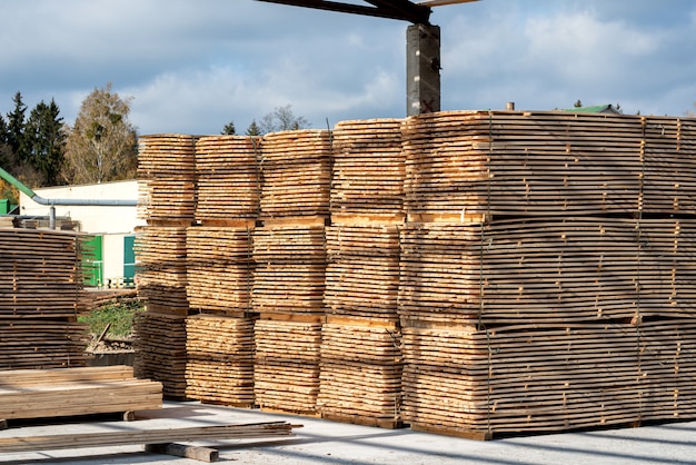 Stapels houten planken in de zagerij, planken. Magazijn voor het zagen van planken op een zagerij buitenshuis. Houten houtstapel van houten spatiesbouwmateriaal. Industrie.