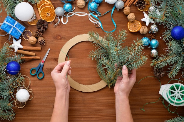 Stapsgewijs proces om thuis een kerstboomkrans te maken van vuren takken, sinaasappels en kerstballen in de zilveren en blauwe kleuren van de stier 2021.