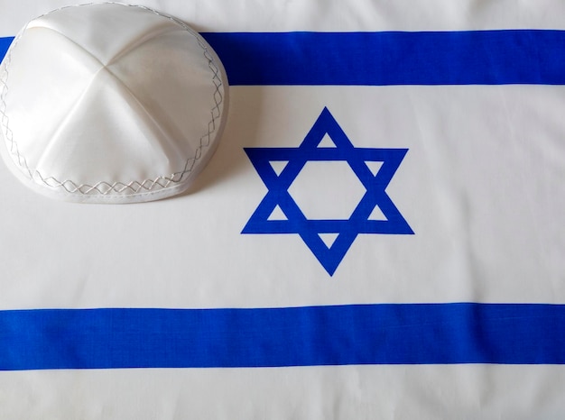 Star of david yarmulke kippa on israeli flag Kippah religious hat with the flag of Israel in the background Still Life of Jewish symbols for Sukkot shabbat rosh hashanah and Yom kippur