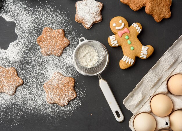 Star shaped baked gingerbread cookies sprinkled with powdered sugar on a black table top view