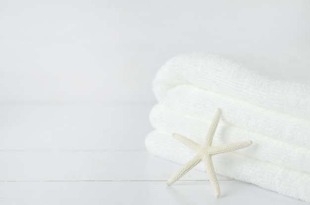 Photo starfish and pile of white towel on white wooden