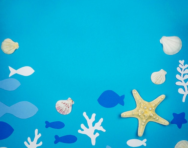 Photo starfish with seashells and fish made of paper on a blue background recreation concept