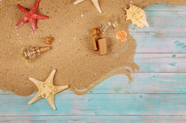 Starfish with seashells on sea sand on blue wooden background. Papyrus from the glass bottle with cork.