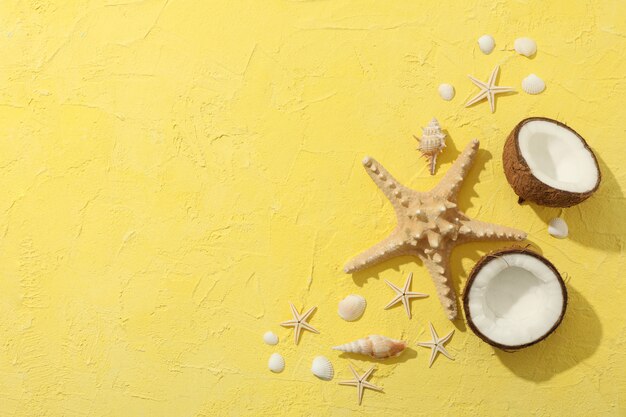 Starfishes, coconut and seashells on yellow, space for text