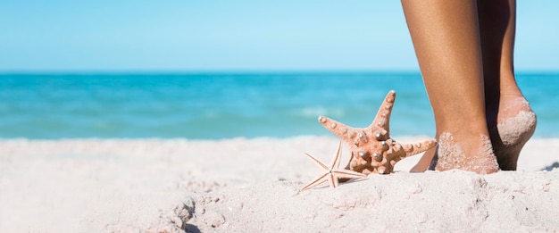 Le stelle marine giacciono accanto ai piedi femminili su una spiaggia sabbiosa banner