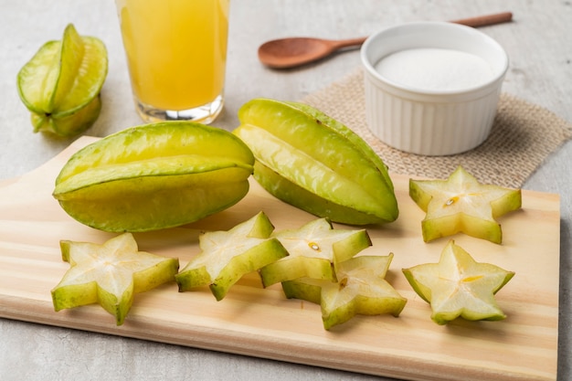 Photo starfruits with slices and juice over a wooden plate.