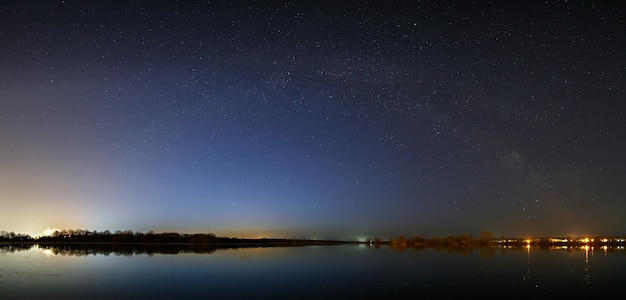 Звезды Млечного Пути в небе перед рассветом. Ночной пейзаж с озером. Панорамный вид на звездное пространство.