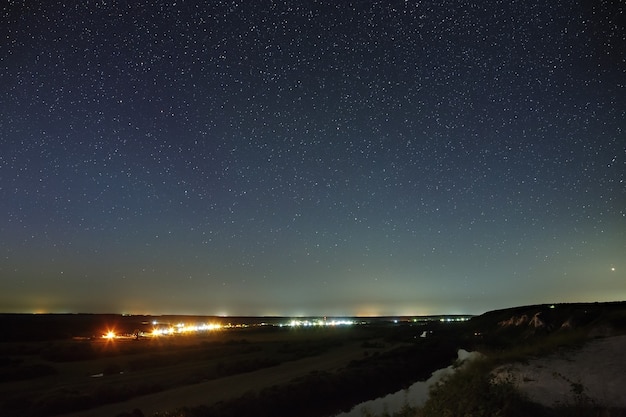 Stars in the night sky over the river valley and city. The cosmic space is photographed on a long exposure.