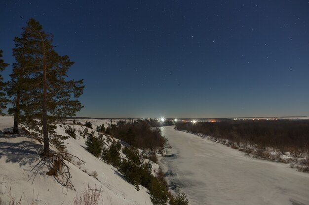 Stars in the night sky. Winter landscape with a frozen river photographed under the full moon.
