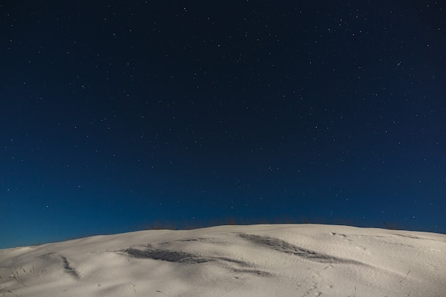 Stars with clouds in the night sky over a snowy mountain ridge. The background of deep space is photographed under the full moon.