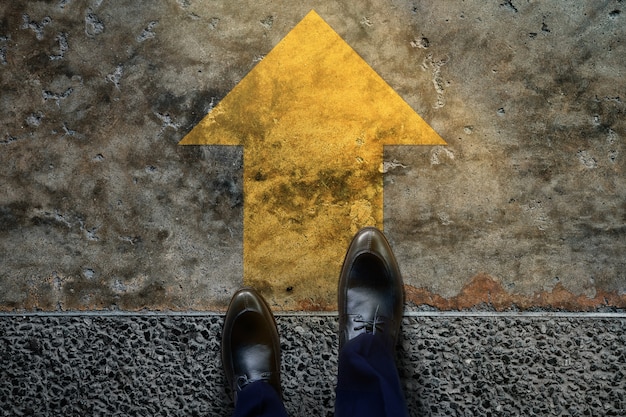 Inizia e sfida il concetto. un uomo d'affari con le scarpe formali passaggi per seguire una freccia gialla, prepararsi ad andare avanti o rischiare il successo. vista dall'alto