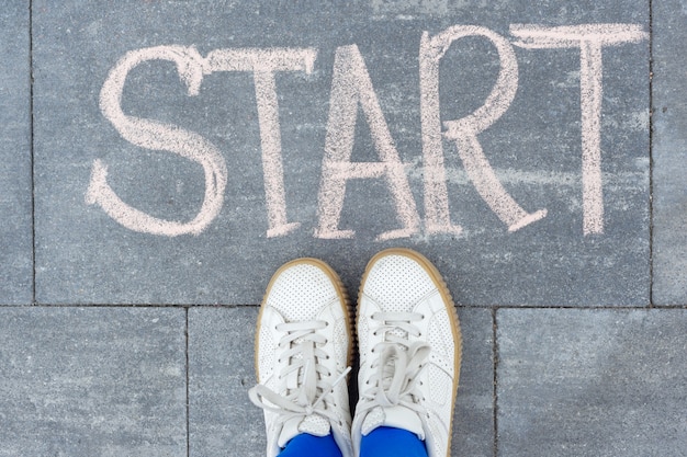 Start concept. Teenager girl standing legs on sidewalk in front of word hand written chalk start. Back to college