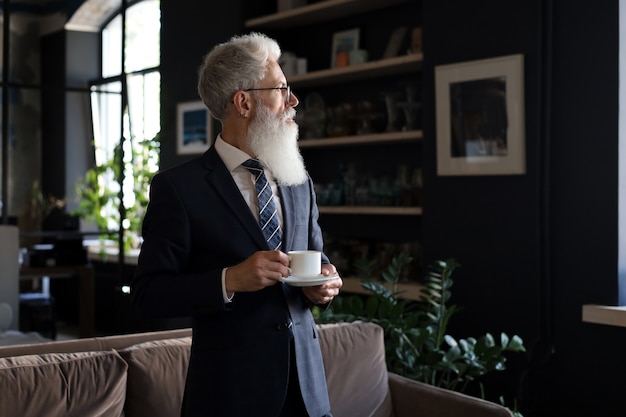 Start of a new working day with a cup of coffee. Handsome mature man holding coffee cup standing in his modern office.