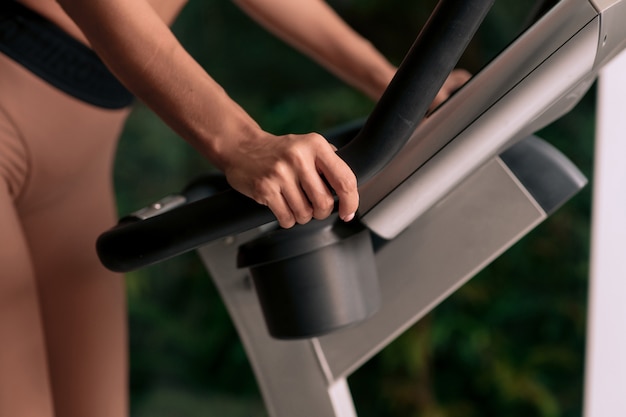 Start running. A close-up photo of a woman in sportswear holding the handle of an exercise bike in the gym with her hands.