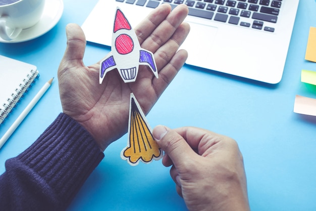 Photo start up concept with rocket in male hand on blue desk