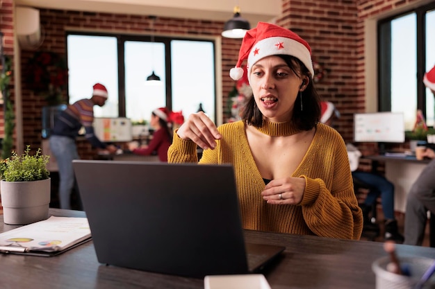 Startende werknemer chatten op videocall-vergadering op het werk, praten op externe videoconferentie-oproep op kantoor met kerstboom. Vrouw die teleconferentiechat gebruikt op feestelijke werkplek.