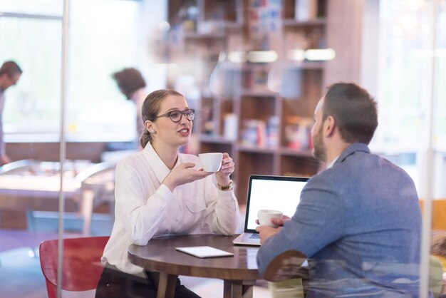 startende zakenmensen die laptop gebruiken om zich voor te bereiden op de volgende vergadering terwijl ze koffie drinken en ideeën bespreken in een creatief kantoor