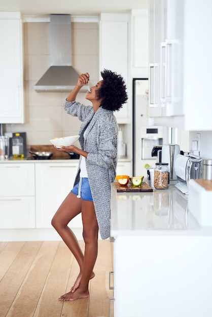 彼女の一日を始める彼女の好きな方法自宅のキッチンに立って朝食を食べているリラックスした若い女性のショット