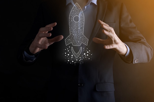 Startup business concept, Businessman holding icon transparent rocket is launching and soar flying out from screen with network connection on dark wall.