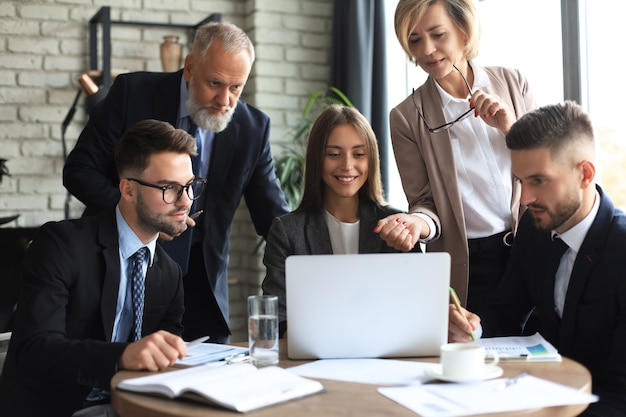 Squadra di affari di avvio sulla riunione nell'interno luminoso moderno dell'ufficio e sul lavoro al computer portatile.