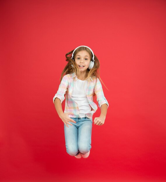 Startup concept small girl in earphones childrens day fun in motion small dancer moving with energy hipster kid relax and jumping energetic child dancing happy childhood kid listen music