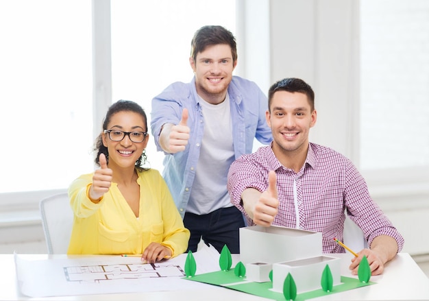 startup, education, architecture and office concept - smiling architects with house model and blueprint in office showing thumbs up