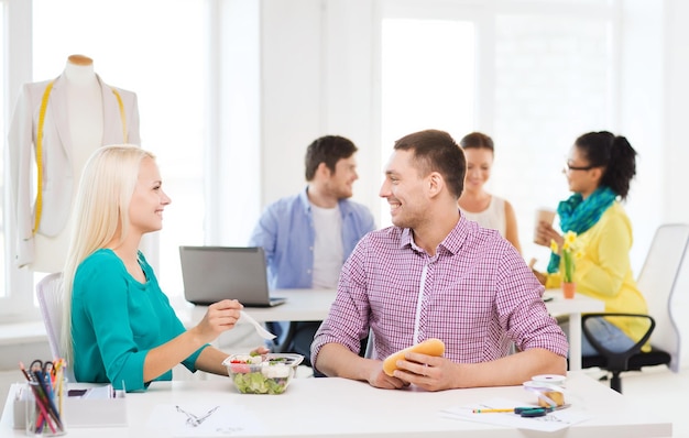 startup, education, fashion, food and office concept - smiling fashion designers having lunch at office