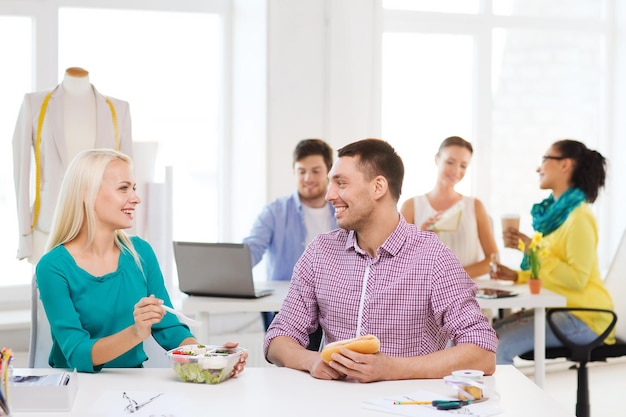 startup, education, fashion, food and office concept - smiling fashion designers having lunch at office