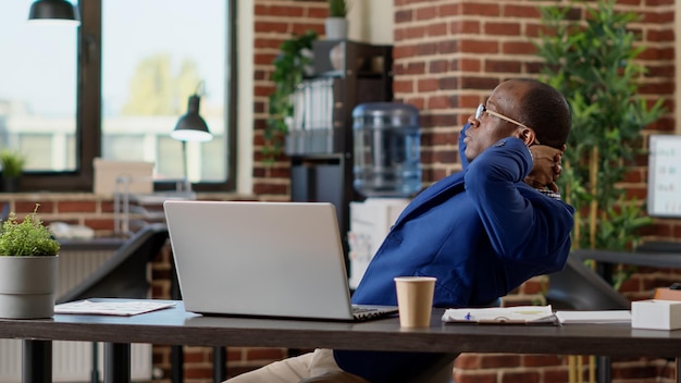 Startup employee relaxing laid back on desk chair in office after working on internet website. Taking break and timeout from paperwork, pausing with hands behind head to relieve stress.