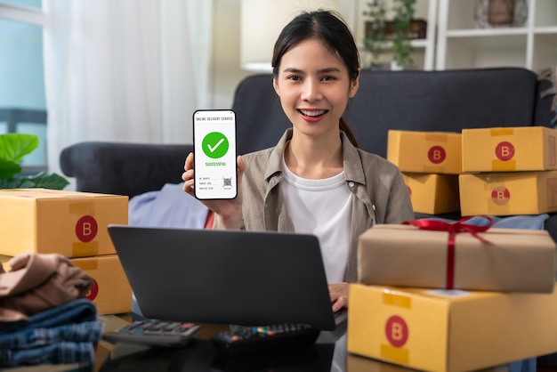 Запуск малого бизнеса, женская рука с помощью смартфона со сканирующим QR-кодом на доставке картонной коробки для отправки продуктов клиентам.