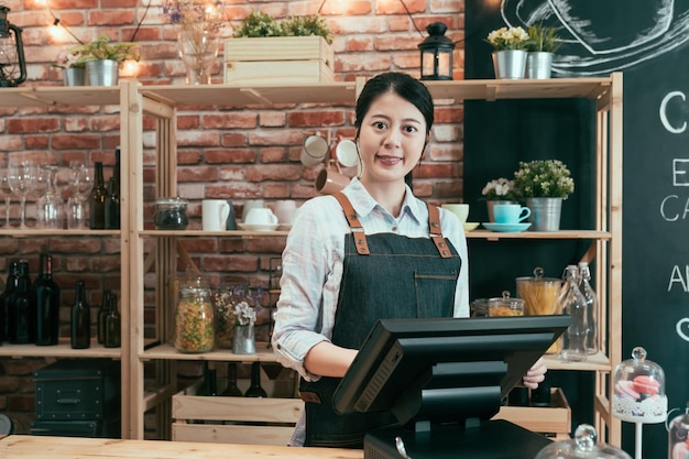 Startup successful small business concept. cafe restaurant owner woman standing in wood counter. Portrait young beautiful lady boss in coffeehouse face camera smiling while working on point terminal