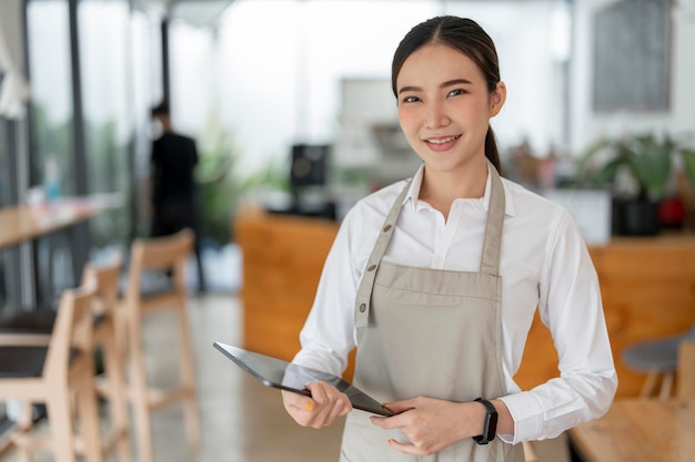 Startup successful small business owner sme beauty girl stand with tablet in coffee shop restaurant Portrait of asian woman barista cafe owner SME entrepreneur seller business concept