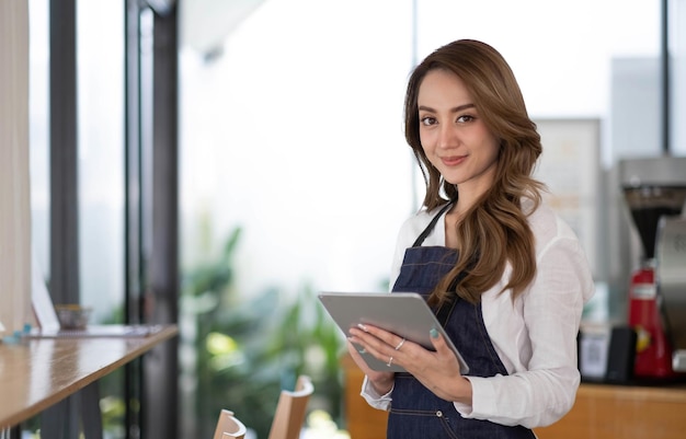 Startup successful small business owner sme beauty girl stand with tablet smartphone in coffee shop restaurant Portrait of asian tan woman barista cafe owner SME entrepreneur seller business concept