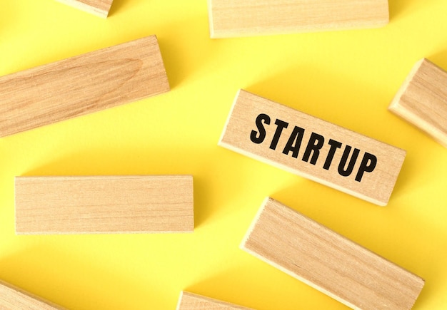 STARTUP text written on a wooden blocks on a yellow background