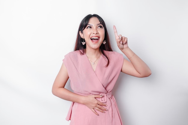 Starving Asian woman dressed in pink pointing at the copy space on top of her isolated by white background