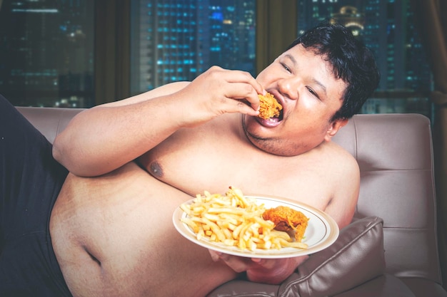 ソファでジャンクフードを食べる飢えたデブ男