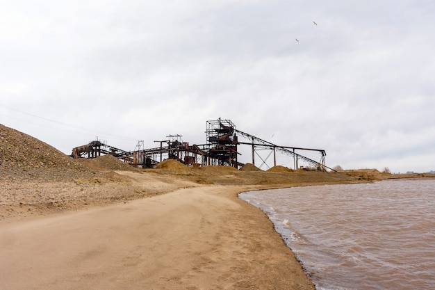 Stationary rusty separator of sand and gravel on the sandy bank of the river