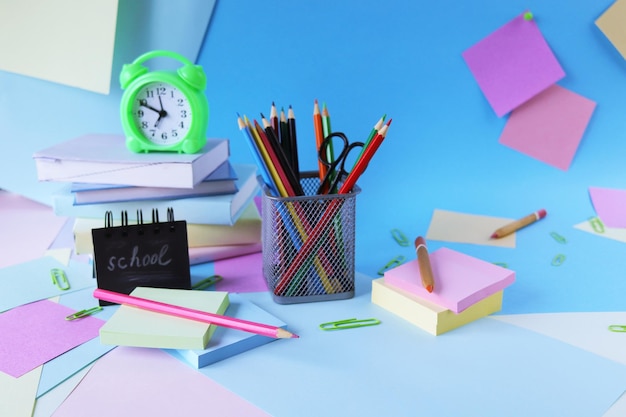 Stationery, alarm clock, books on a background of pastel colors of multi-colored paper